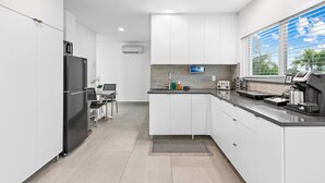 A modern kitchen with white cabinets, a black refrigerator, a coffee maker, and a window with blinds. - Apt W/patio, Balcony & Mini-golf (Deerfield Beach)