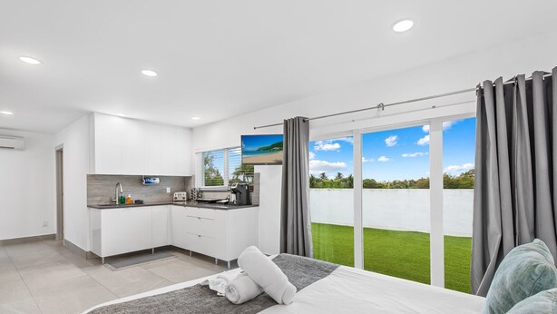 A modern hotel room with a large bed, a kitchenette, and a balcony with a view of the sea. - Apt W/patio, Balcony & Mini-golf (Deerfield Beach)