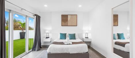 A modern bedroom with a large bed, a sliding glass door to a garden, and a large mirror.