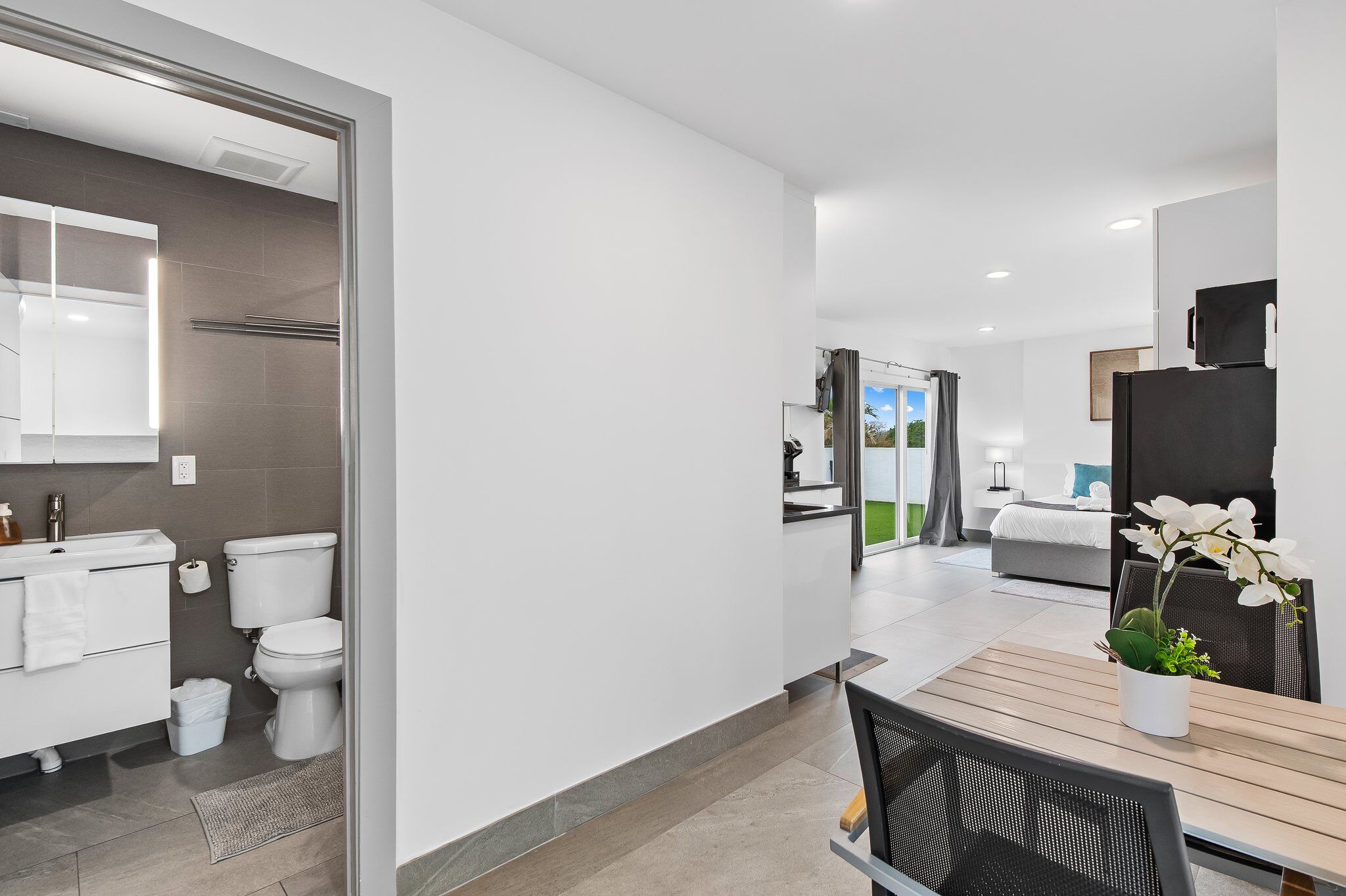 A modern hotel room with a bathroom, a dining area with a table and chairs, and a bed with a view.