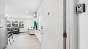 A modern kitchen with a refrigerator, a dining area with a sofa and table, and a view through the window.
