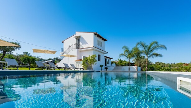 Un bâtiment moderne doté d’une piscine, de chaises longues et de palmiers.