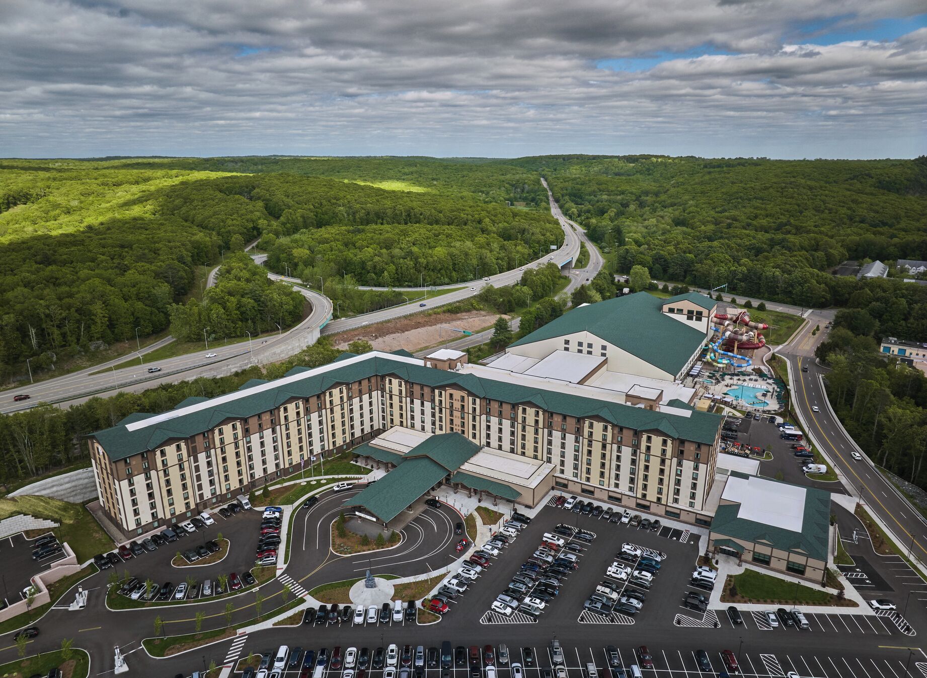 A large hotel with multiple floors, a parking lot, and a swimming pool area.
