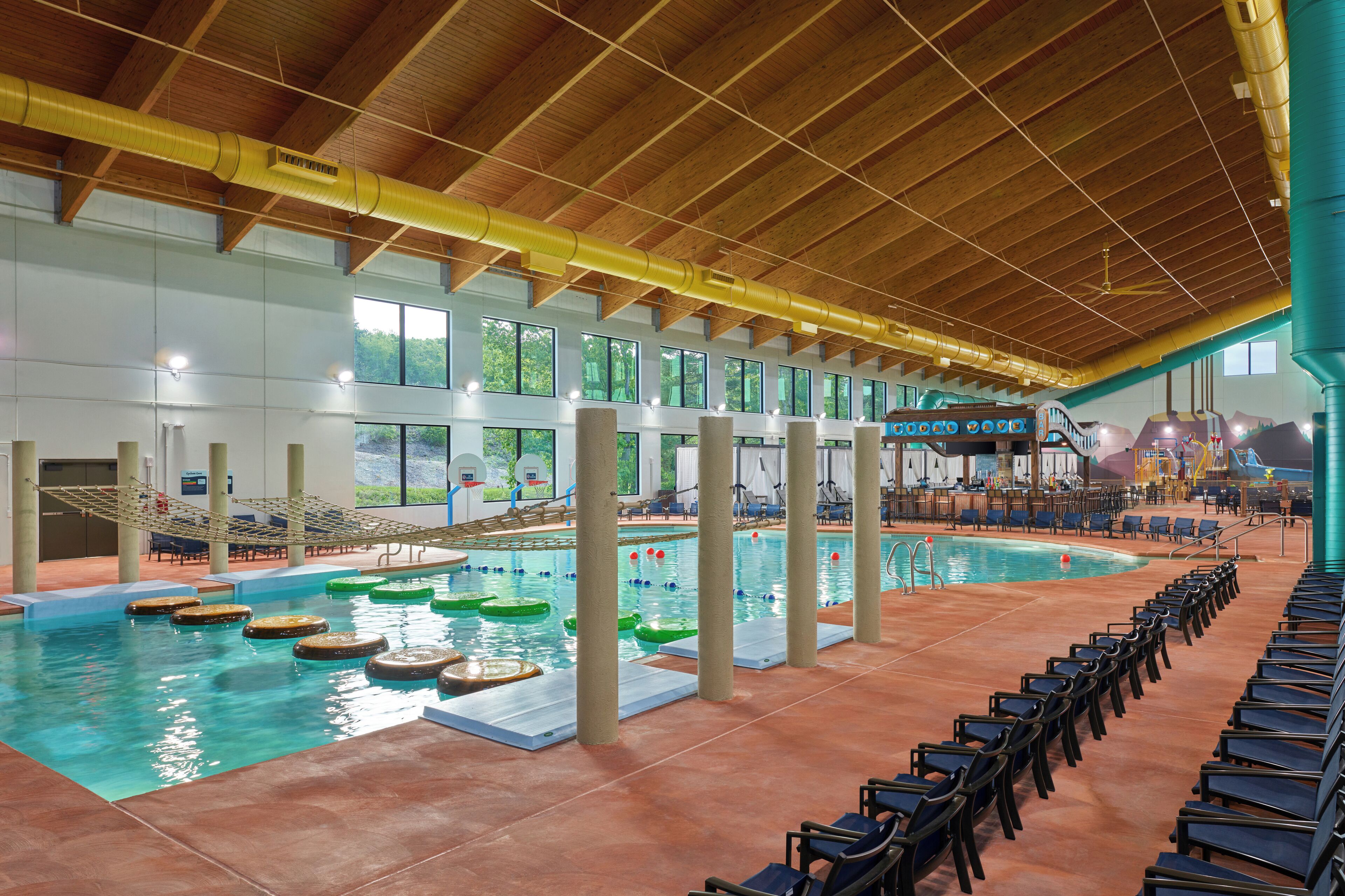 An indoor swimming pool with multiple lanes, a diving board, and a seating area with chairs.