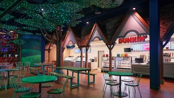 An indoor dining area with green tables and chairs, a Dunkin' Donuts counter, and a ceiling with hanging lights.