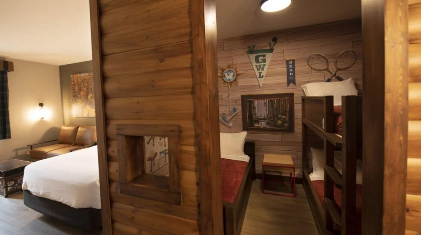 A room with a bed, a small table, a fireplace, and a shelf with books and a tennis racket.