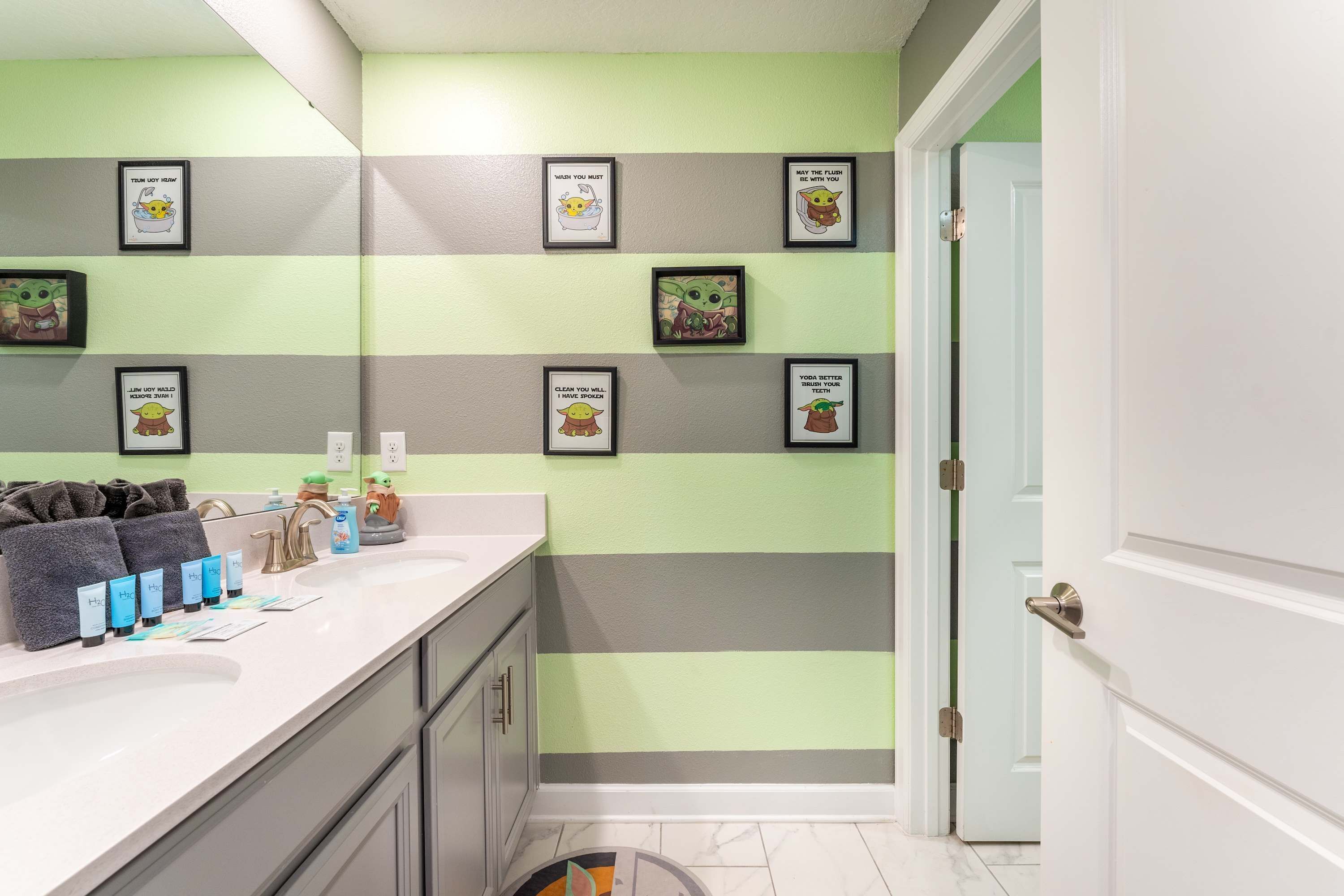 A bathroom with a striped wall design, a sink with toiletries, and framed pictures on the wall.