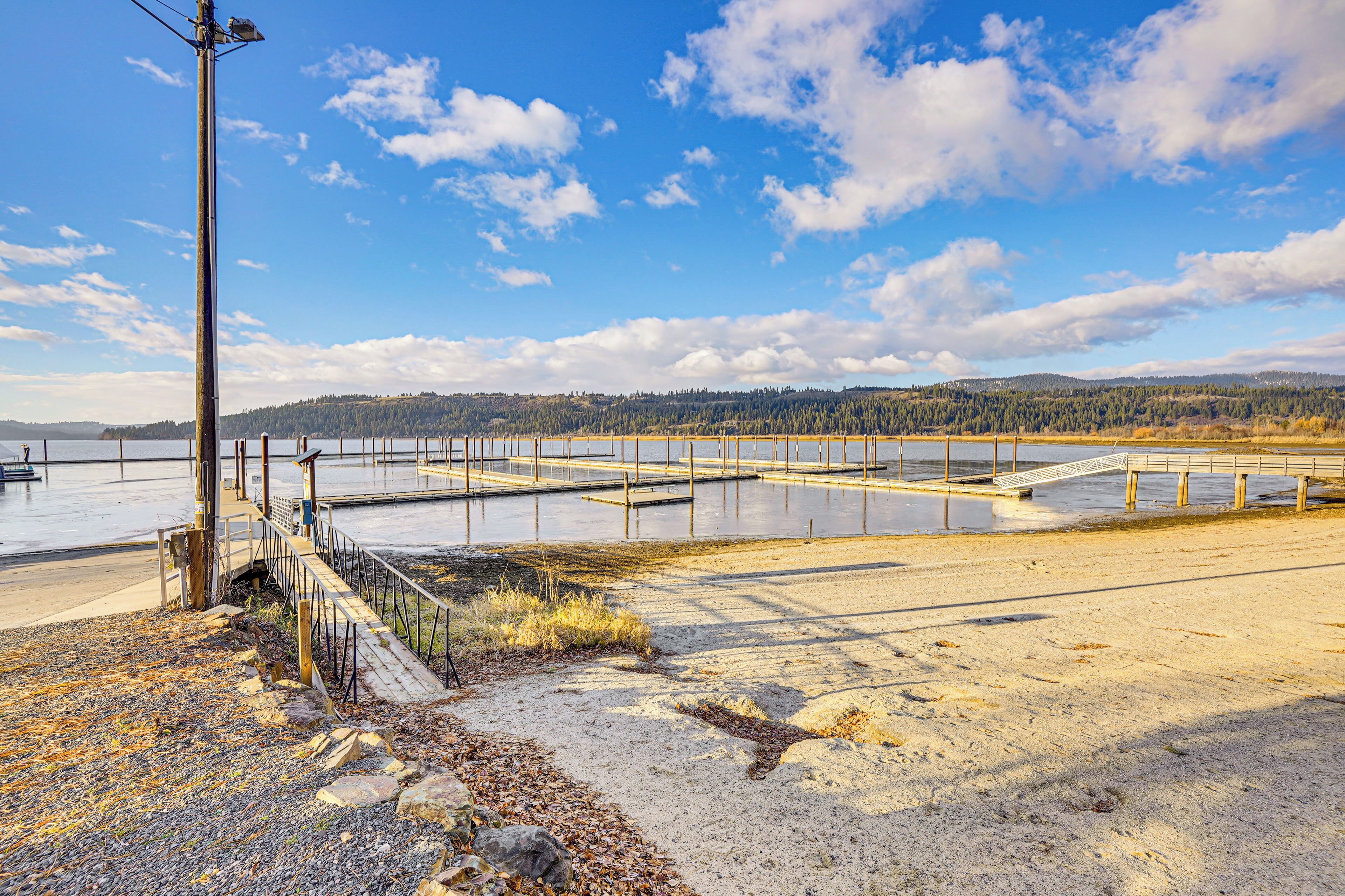 A beach with a wooden pier, a rocky shoreline, and a forested hill in the background.