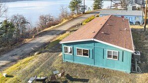 A blue house with a red roof, a gravel driveway, and a view of a lake. - Walk to Marina: Harrison Cabin w/ Lake View! (Harrison)