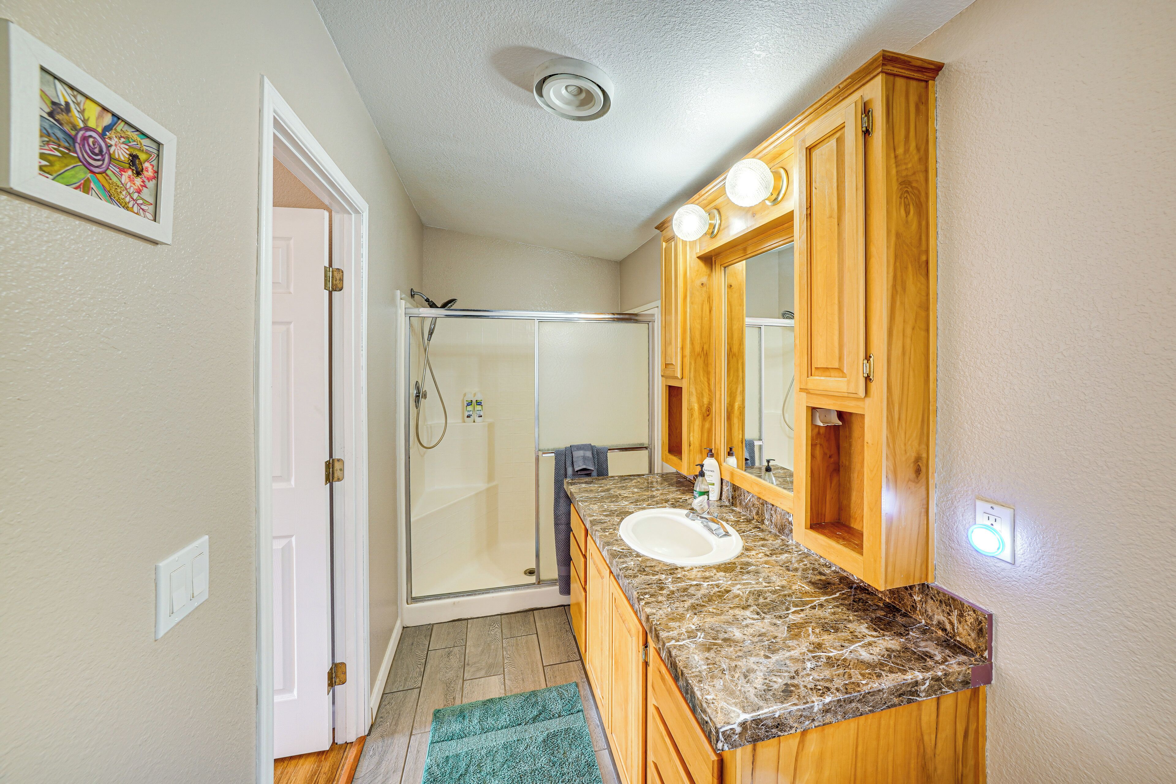 A bathroom with a shower, a sink, wooden cabinets, and a mirror.