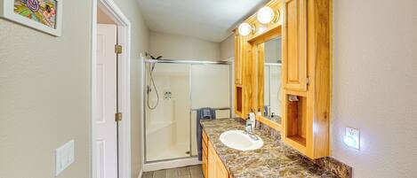 A bathroom with a shower, a sink, wooden cabinets, and a mirror.