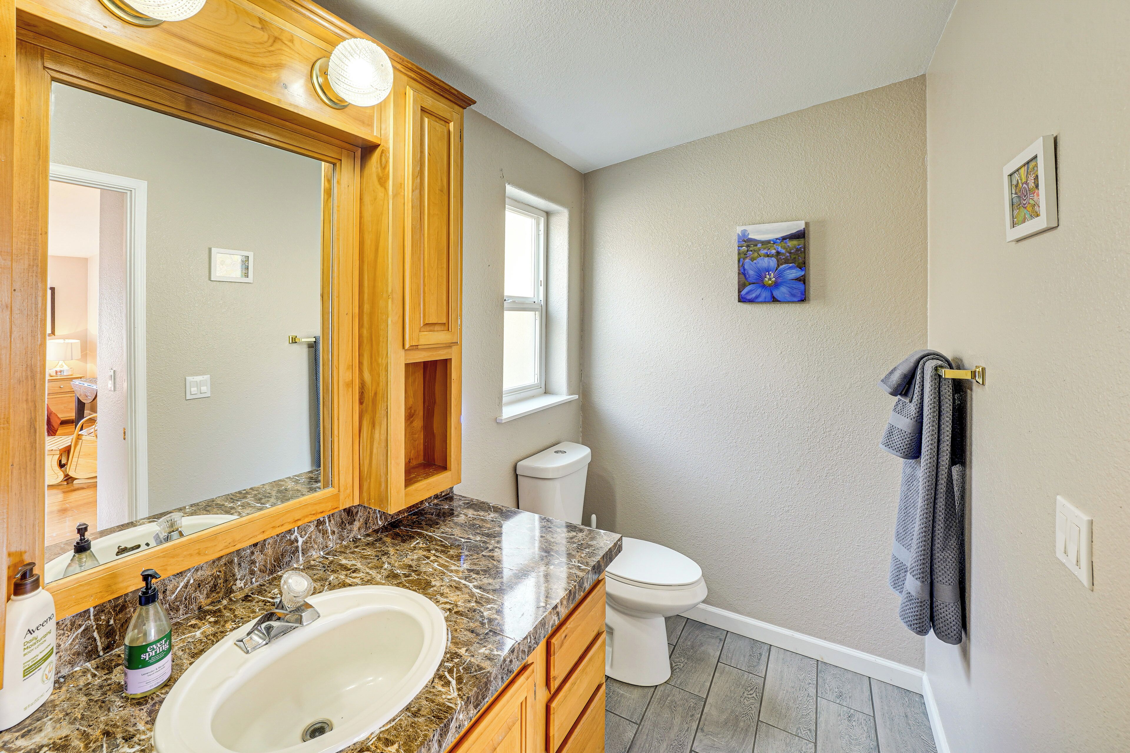 A bathroom with a marble sink, wooden cabinets, a white toilet, and a window.