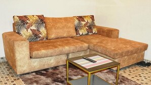 Ein braunes Sofa mit gemusterten Kissen, ein Couchtisch mit Glasplatte und ein Fellteppich.