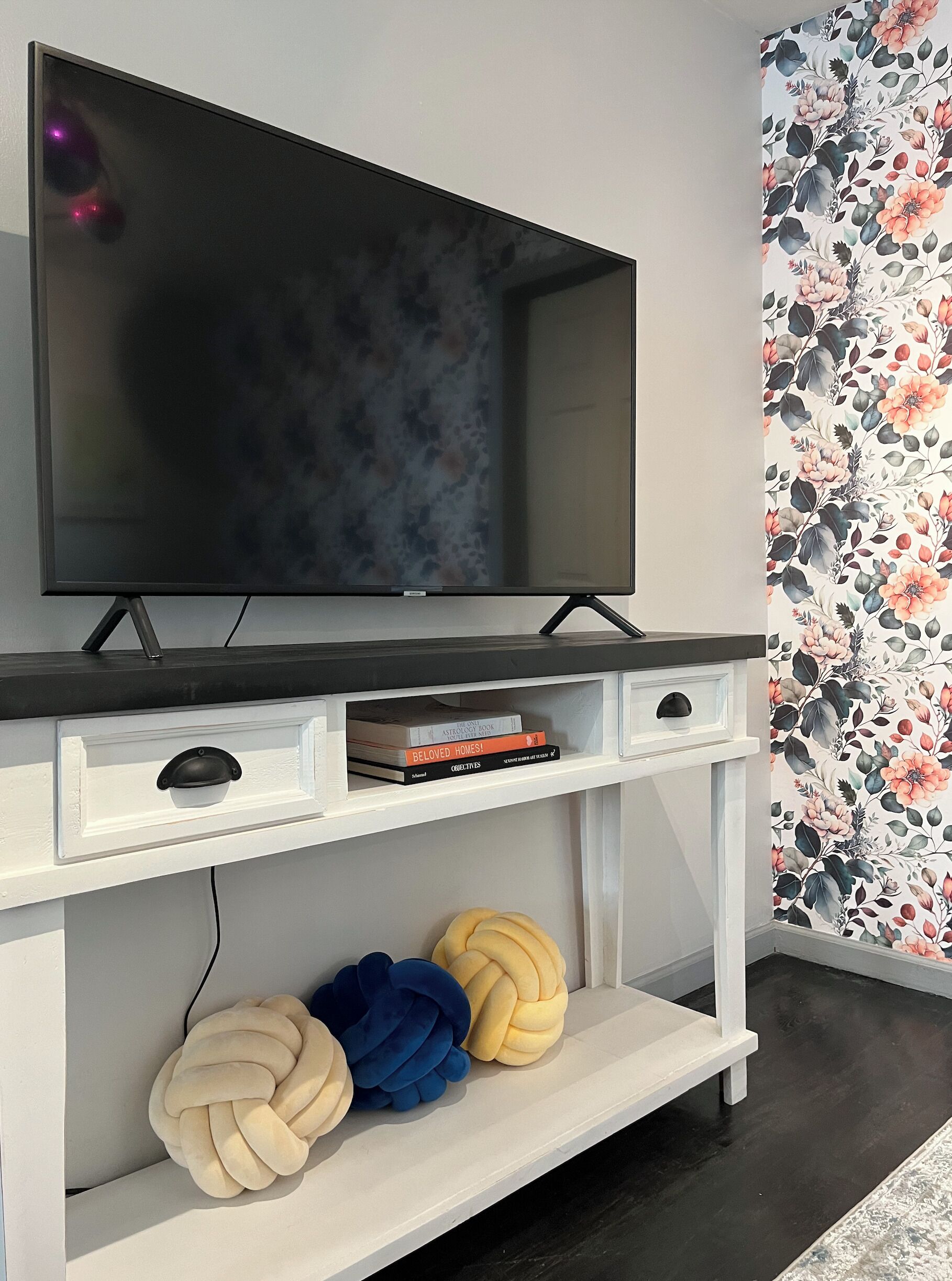 A modern living room with a flat-screen TV on a white TV stand, a bookshelf with books, and decorative pillows.