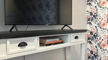 A modern living room with a flat-screen TV on a white TV stand, a bookshelf with books, and decorative pillows.