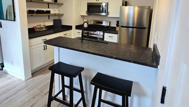 Een moderne keuken met witte kasten, roestvrijstalen apparatuur en zwarte barkrukken.