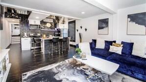 A modern kitchen with a marble backsplash, a dining area with a white table and blue sofa, and a living room with dark flooring and a large rug. - Heated Pool, Spa (Clearwater)