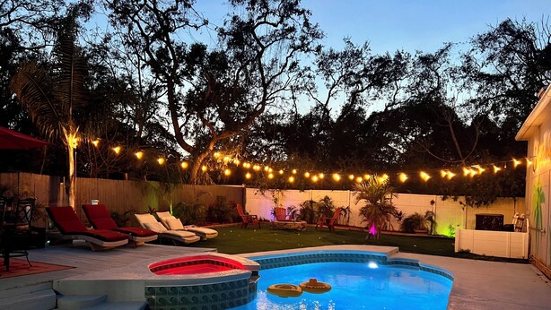 A backyard with a swimming pool, lounge chairs, and string lights. - Heated Pool, Spa (Clearwater)