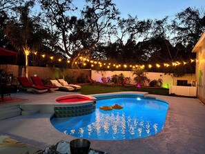 A backyard with a swimming pool, lounge chairs, and string lights. - Heated Pool, Spa (Clearwater)
