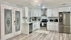 A modern kitchen with white cabinets, a stainless steel refrigerator, a microwave, and a stove. - Heated Pool, Spa (Clearwater)