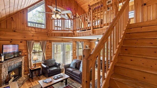 A wooden cabin interior with a fireplace, a sofa, a television, and a staircase. - Bear Hideaway (Sevierville)