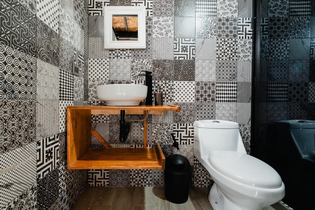 A bathroom with a white toilet, a wooden shelf with a sink, and patterned tiles on the walls.