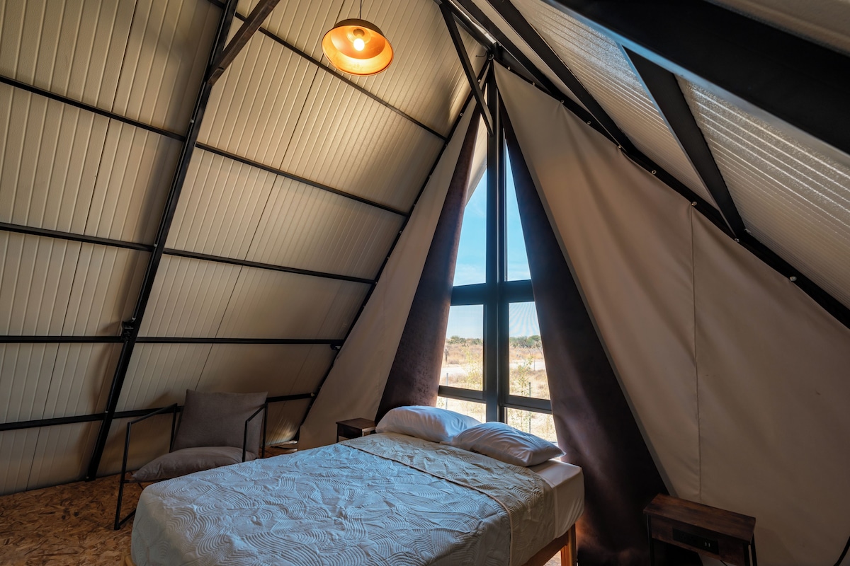 Una habitación acogedora de forma triangular con cama, almohadas, una mesita pequeña y una lámpara colgante.