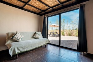 A room with a sofa, a large window, and a view of an outdoor area with a picnic table. - La Campiña Glamping Club (El Llano)