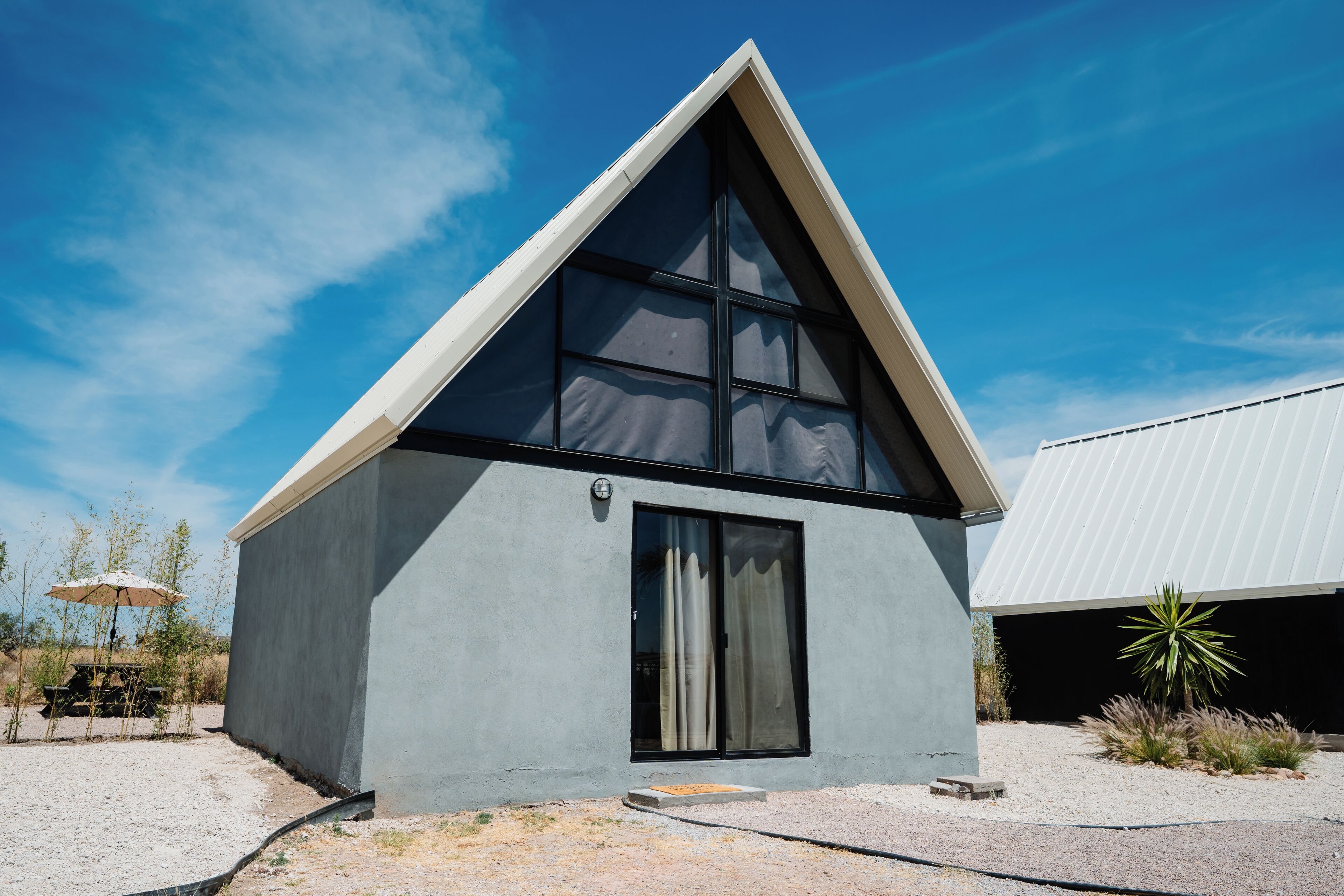 A modern house with a triangular roof, large windows, and a gravel driveway.