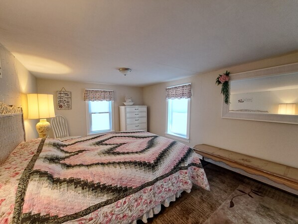 A bedroom with a large bed, a dresser, a chair, and a mirror on the wall.