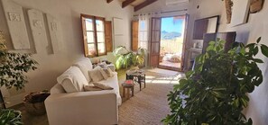 Un saló acollidor amb un sofà, una taula petita i una televisió. Hi ha plantes i una finestra amb cortines.