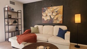 Een woonkamer met een witte bank, een ronde salontafel, een boekenkast en een schilderij van bloemen aan de muur.