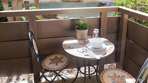 Een terras met twee stoelen en een tafel, omringd door planten en een kleine waterpartij.
