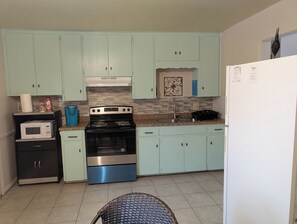 A compact kitchen with light green cabinets, a stainless steel stove, a microwave, and a sink. -  3-bedroom Home away from home while in Rockdale A (Rockdale)