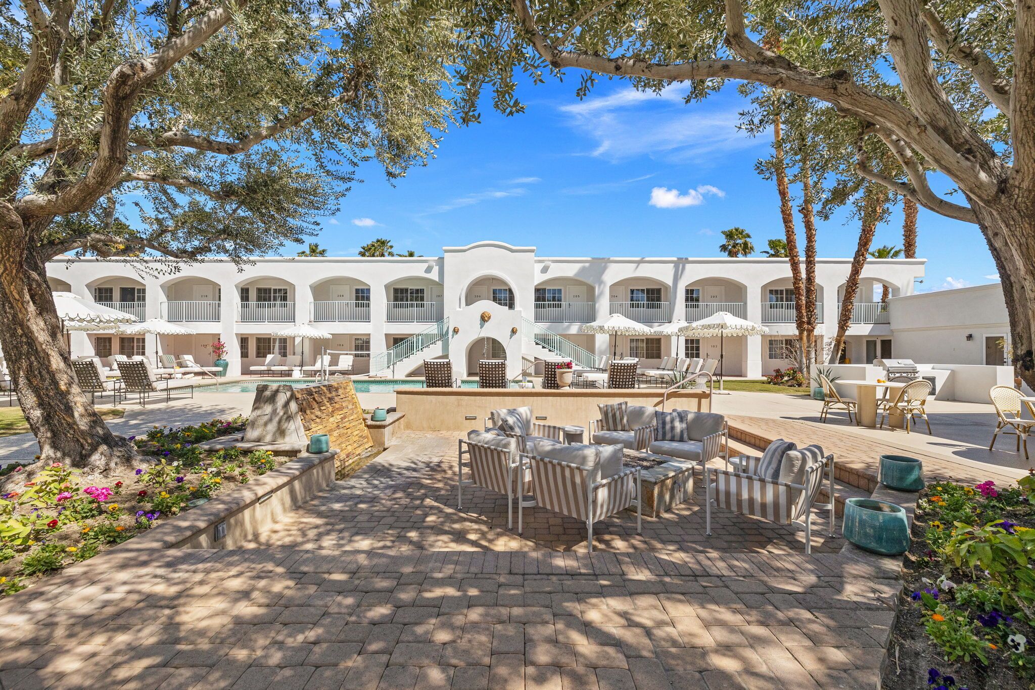 A resort with a pool, outdoor seating, and a white building with arches.