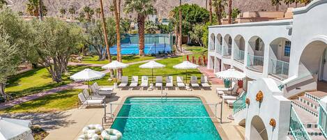 A pool area with lounge chairs and umbrellas, surrounded by palm trees and mountains.