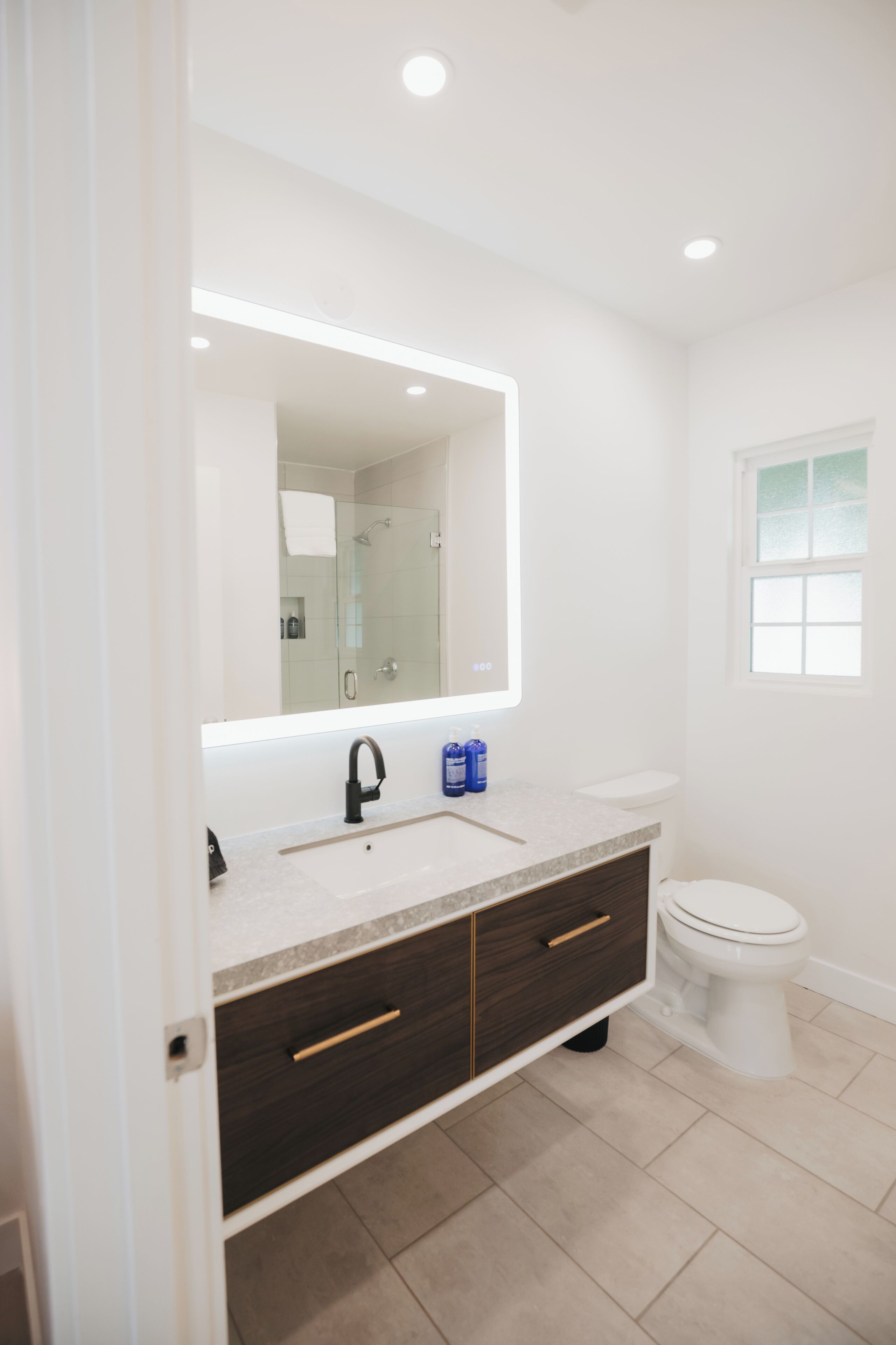 A modern bathroom with a large mirror, a sink, a toilet, and a window.
