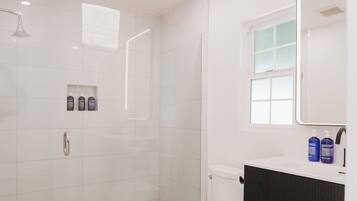 Un baño moderno con ducha de vidrio, inodoro y tocador con espejo.
