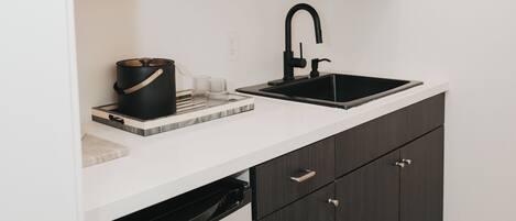 A compact kitchen with a black dishwasher, a black sink, and a wooden shelf above.