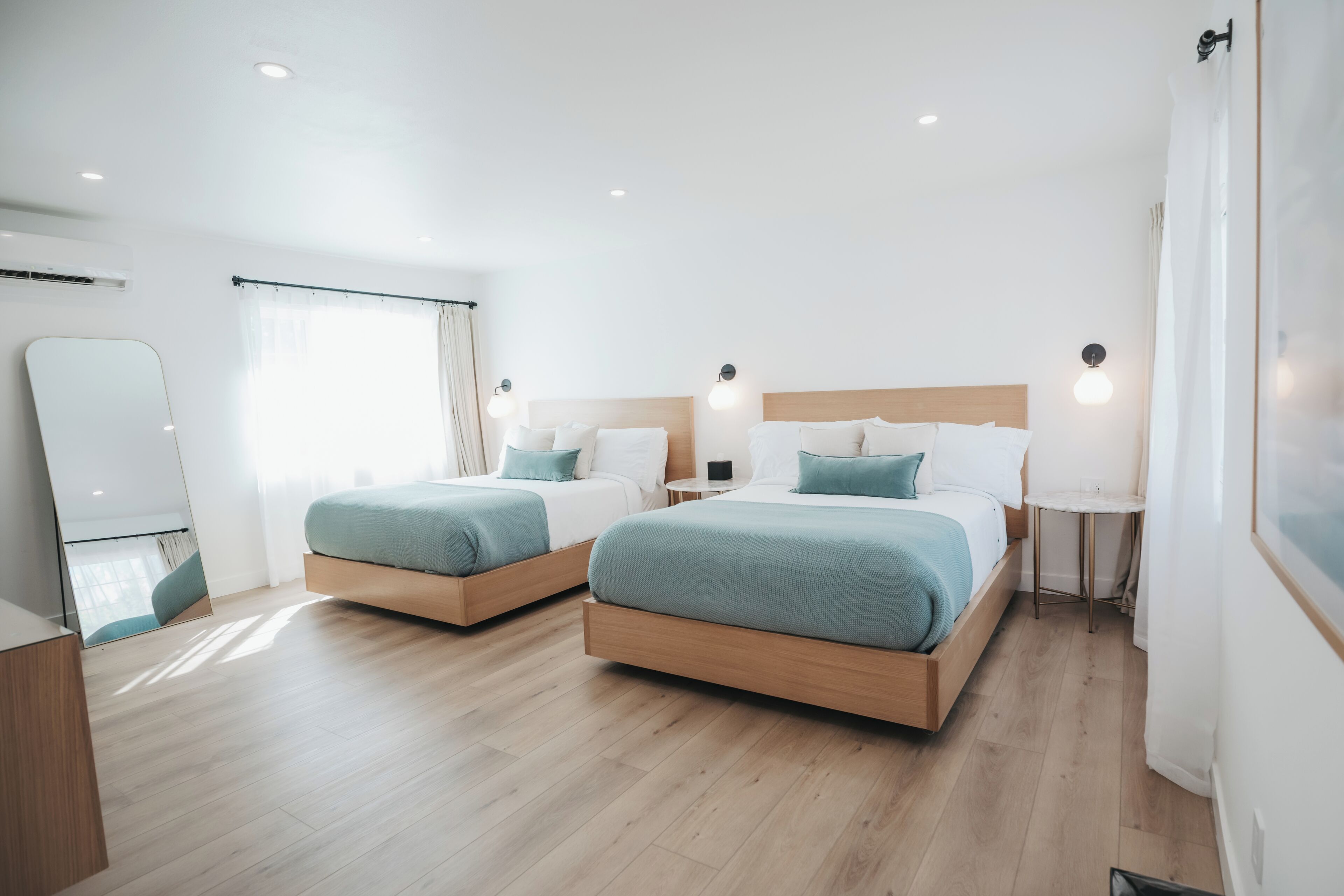A modern hotel room with two beds, a small table, and a mirror.