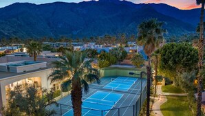 Un campo da tennis circondato da palme e edifici, con montagne sullo sfondo.
