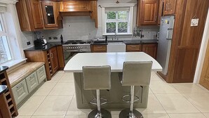 Une cuisine moderne avec des meubles en bois, un îlot central doté de tabourets, un four encastré et un réfrigérateur.
