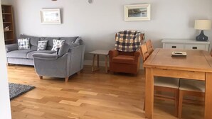 Un salon avec un canapé gris, une table à manger en bois et une petite table d’appoint.