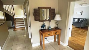 Un couloir avec une console en bois, un miroir et une lampe. Au fond, on aperçoit un escalier menant à une autre pièce.