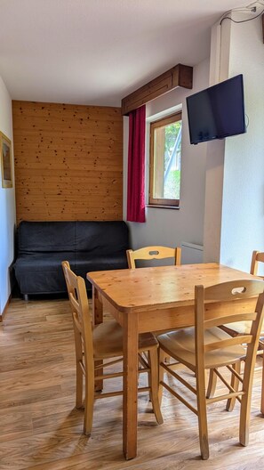 A cozy room with a wooden table and chairs, a black sofa, and a TV mounted on the wall.