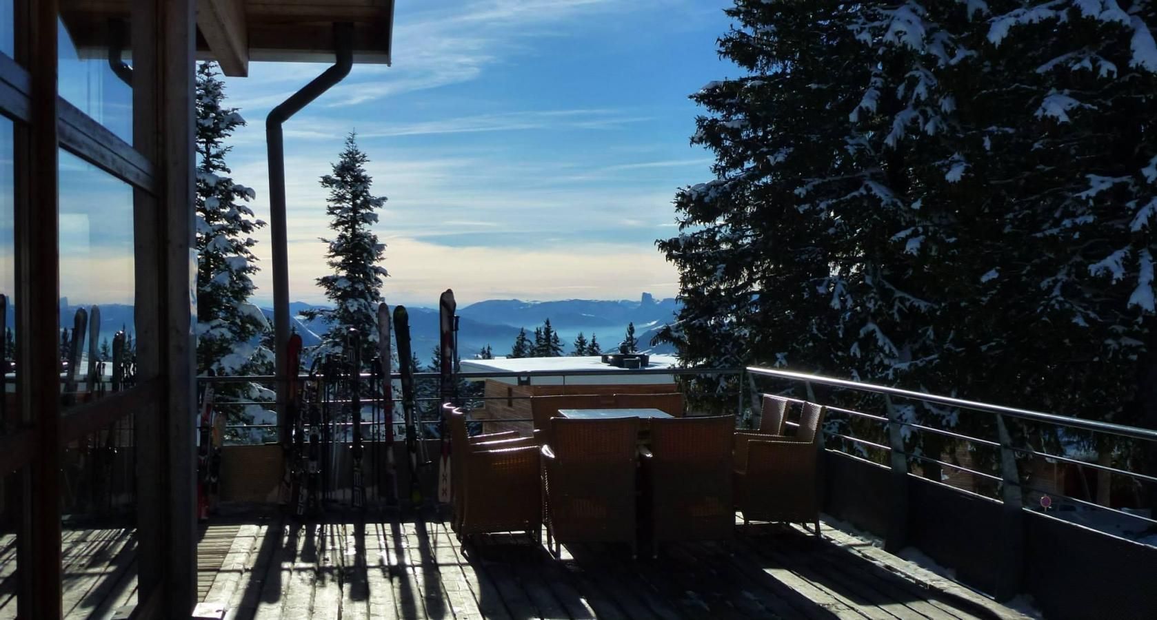 A wooden deck with a view of snow-covered trees and mountains.