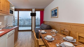 Een gezellig eetgedeelte met een houten tafel voor vier personen, een bank en een keuken met een magnetron en gootsteen.