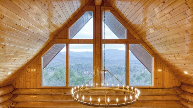 Interior de una cabaña de troncos con un amplio ventanal que ofrece vistas a la montaña, un candelabro y paredes de madera.