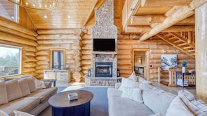 A log cabin interior with a stone fireplace, wooden walls, a sofa, and a television. - Sleeps 21 Luxury Cabin w/ Panoramic View, Hot Tub, Game Room Pinnacle Chalet (Gatlinburg)