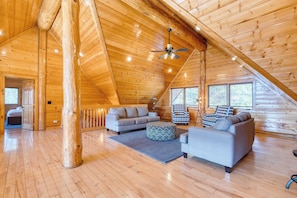 A spacious loft with wooden floors and a sloped ceiling, featuring a sofa set, ottoman, and a ceiling fan. - Sleeps 21 Luxury Cabin w/ Panoramic View, Hot Tub, Game Room Pinnacle Chalet (Gatlinburg)